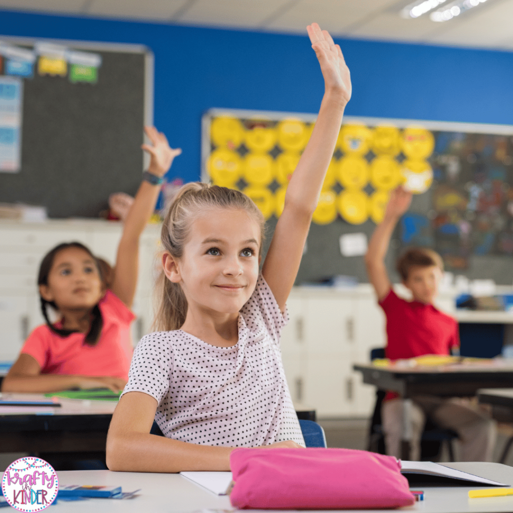 This image shows a group of elementary aged students sitting at their desks and raising their hands.